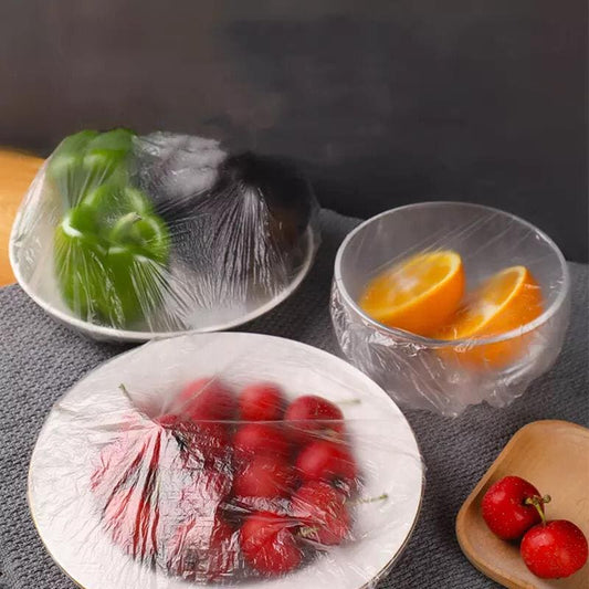 Fruits and vegetables wrapped in clear plastic wrap on a dark surface.